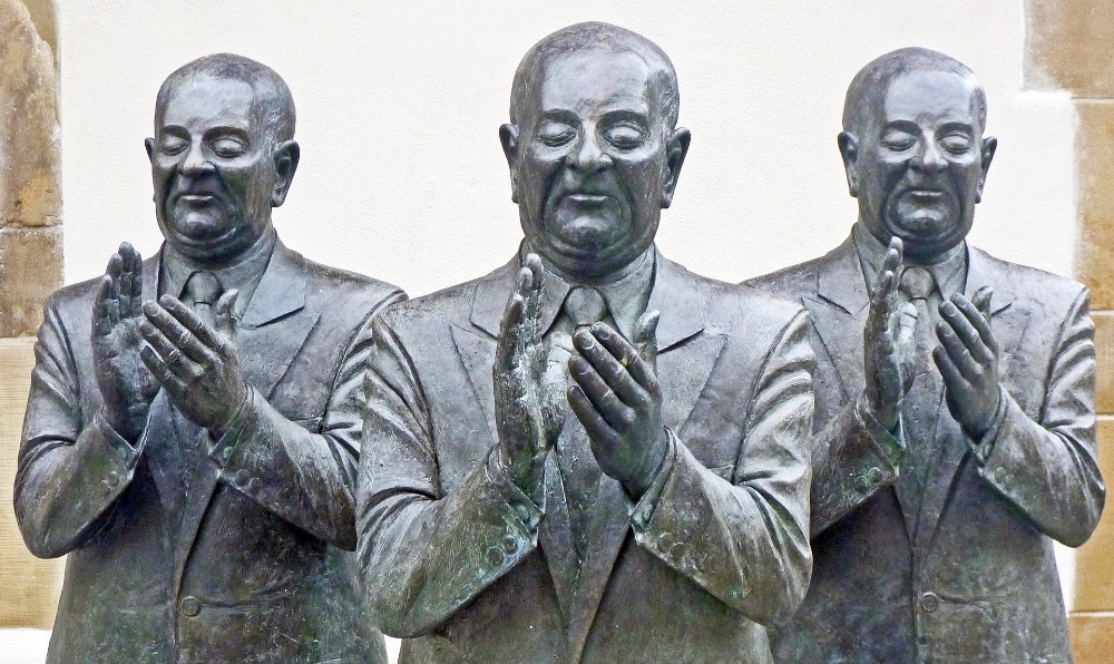 sculpture of 3 dour men applauding awkwardly